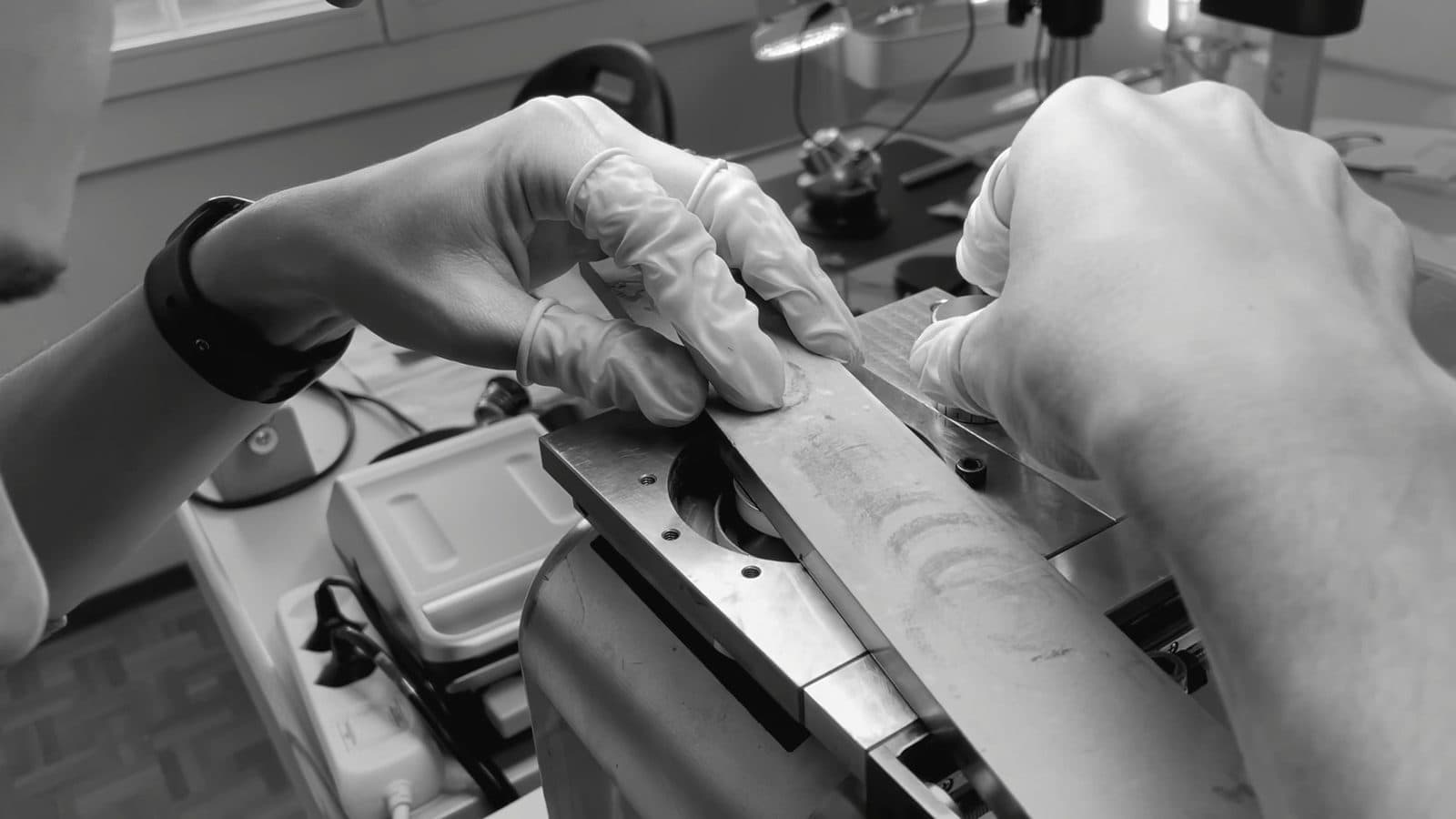 Mains gantées guidant une pièce sur un outil de terminaison, à l'établi